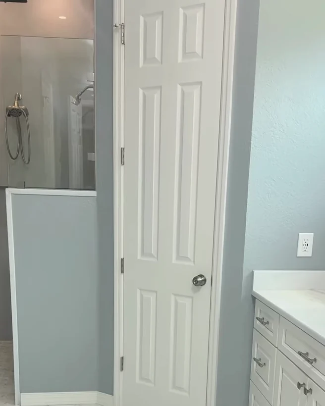 Master bathroom remodel in Sorrento, FL: glass walk-in shower behind a half wall, white vanity cabinetry and marble-look tile floor