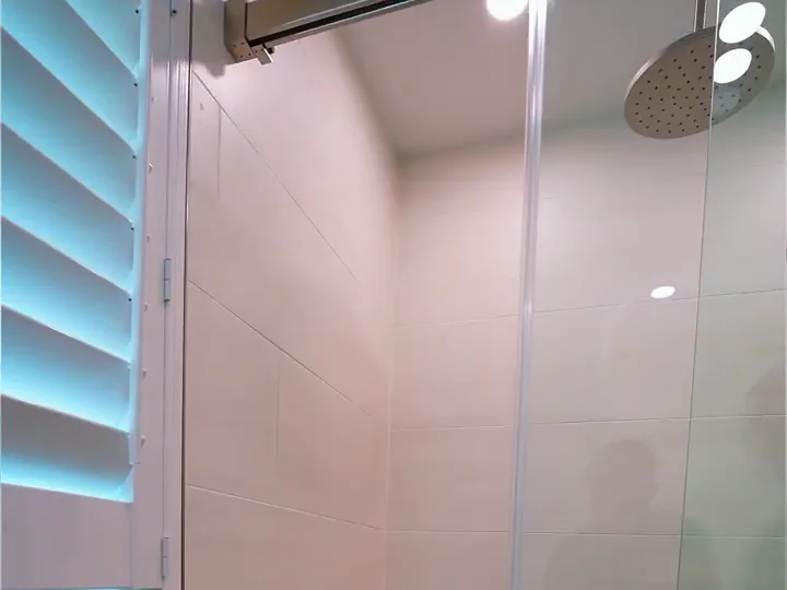Walk-in shower remodel in Orlando, FL with a barn-door style glass enclosure, rain shower head and large-format porcelain wall tile