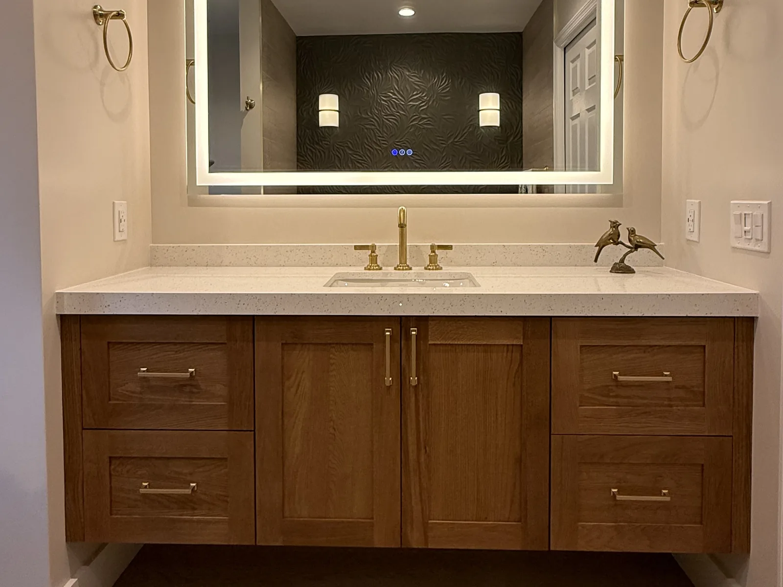 Floating wood vanity with a quartz top, brass fixtures and a backlit LED mirror in a Posada Remodeling & Design bathroom remodel