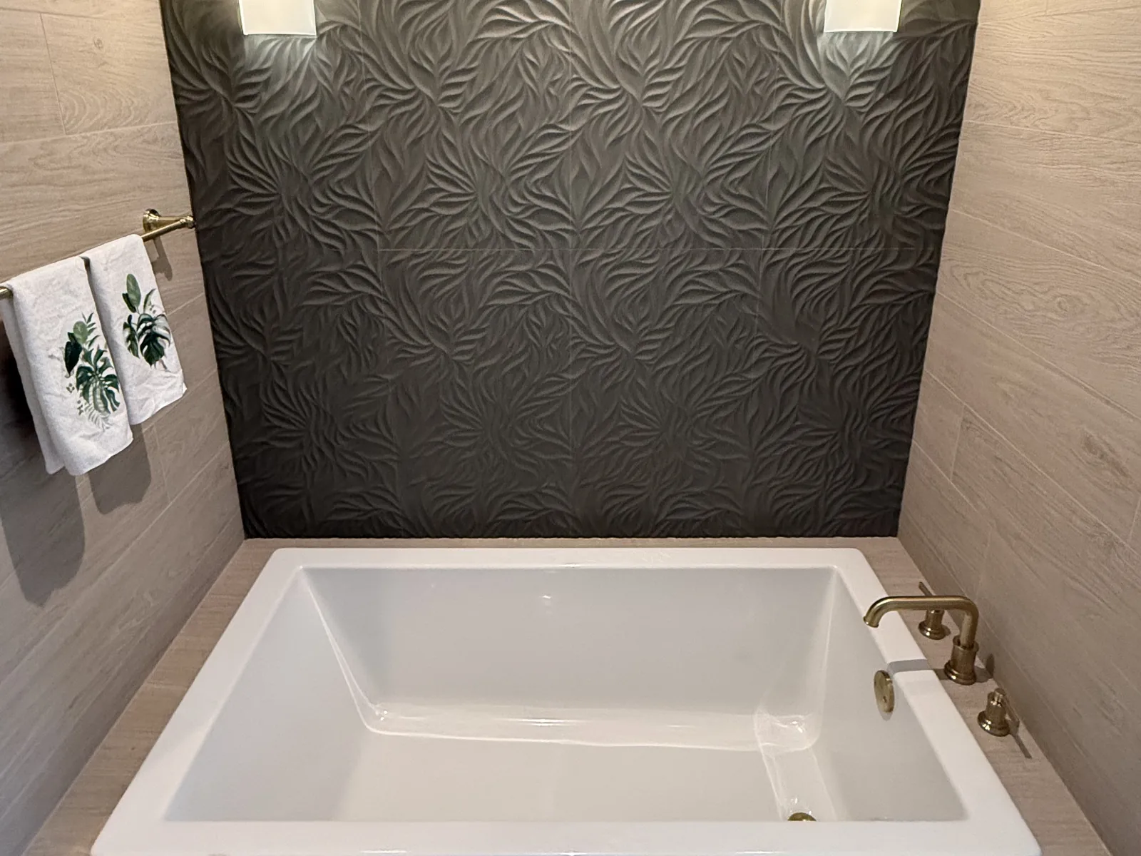 Bathroom remodel with a deep soaking tub, textured dark accent wall and brushed brass tub filler by Posada Remodeling & Design