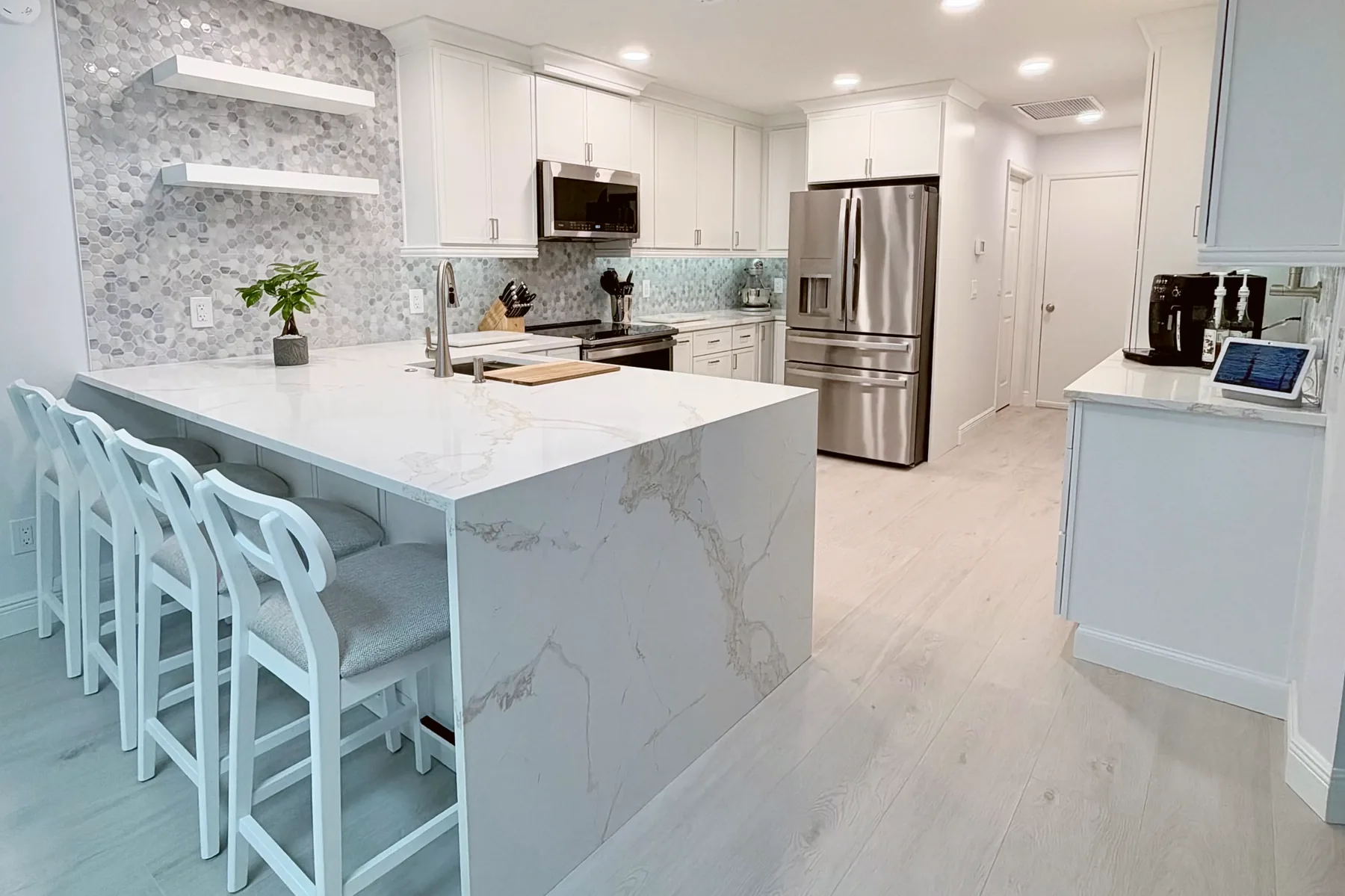 Kitchen remodel by Posada Remodeling & Design with a waterfall quartz island, white shaker cabinets and a marble mosaic backsplash in Central Florida