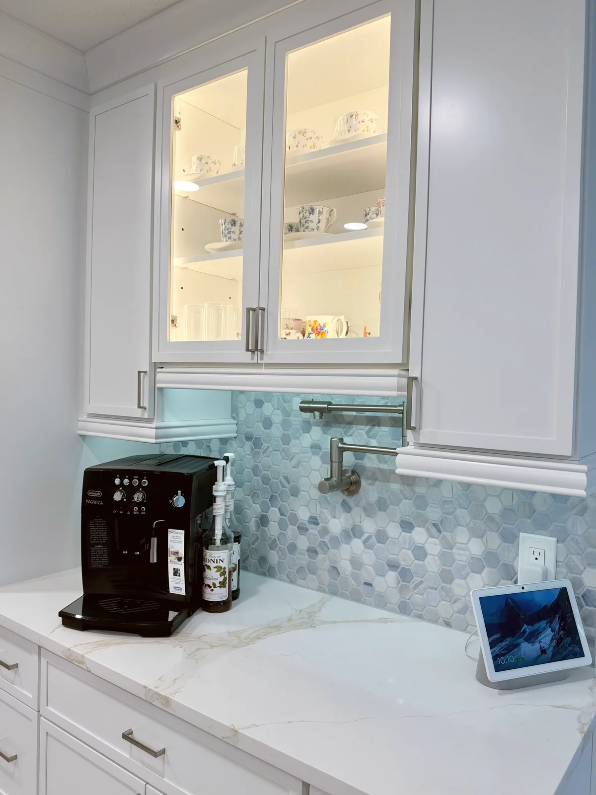 Lit glass-front cabinets over a coffee station with a pot filler and marble hexagon backsplash in a Posada Remodeling & Design kitchen remodel
