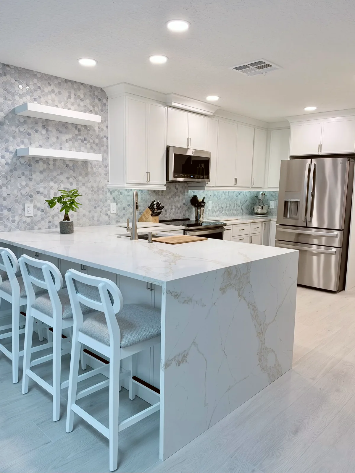 Kitchen remodel with a waterfall quartz island, white counter stools and white shaker cabinets by Posada Remodeling & Design in Central Florida