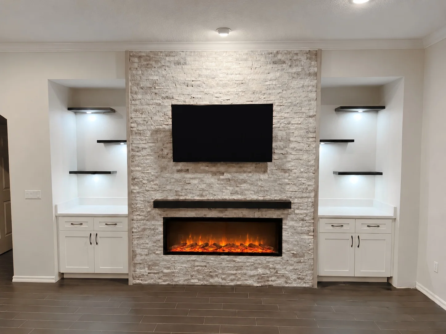Floor-to-ceiling stacked-stone fireplace with a linear electric fireplace, white built-in cabinets and lit floating shelves, by Posada Remodeling & Design