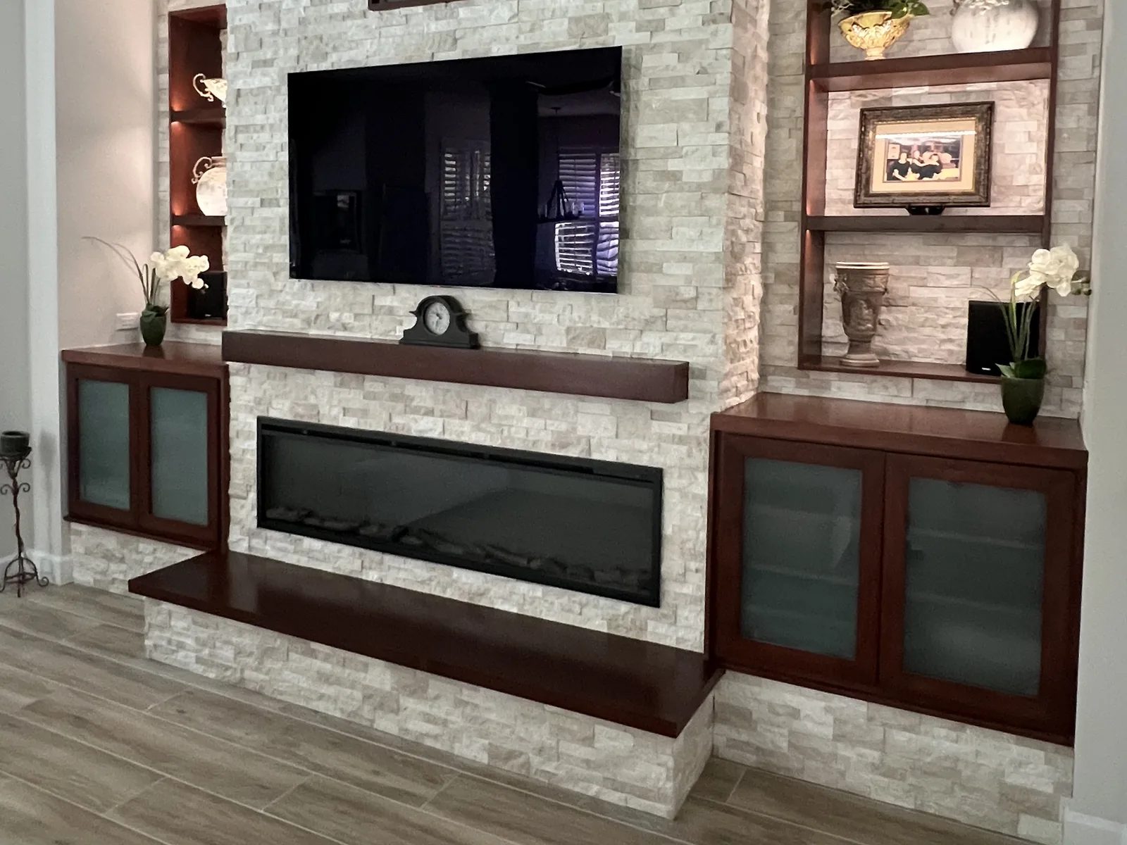 Stacked-stone fireplace feature wall with a linear electric fireplace, lit built-in shelves and wood-look tile floors by Posada Remodeling & Design